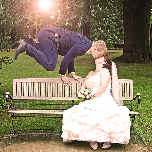 Hochzeitsfotograf Dresden - Ein Bräutigam springt über eine Bank und küsst dabei seine Braut. Die Sonne scheint durch die Äste der Bäume im Hintergrund.