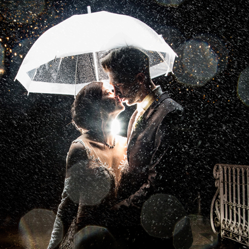 Hochzeitsfotograf Dresden - Ein Brautpaar steht im Regen unter einem Schirm mit Hintergrundlicht.