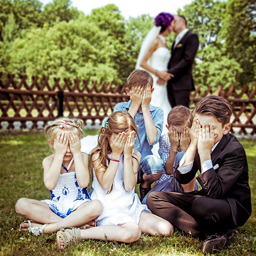 Hochzeitsfotograf Dresden - die Kinder im Vordergrund halten sich die Augen zu, während im Hintergrund das Brautpaar küsst.